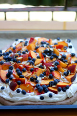 Chocolate Pavlova cake with whipped cream, peaches, blueberries and almonds. Selective focus.