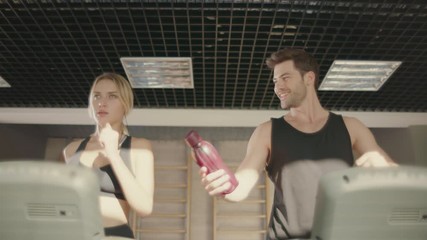 Handsome man flirting with woman on treadmill machine in fitness club.