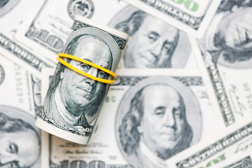 A roll of 100 dollar bills close-up on a pile of American dollars. Background from banknotes of 100...