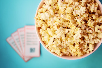 Fresh tasty unhealthy popcorn in big bucket, movie tickets laying near on table