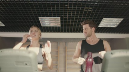 Joyful fitness couple talking on treadmill machine in gym club.