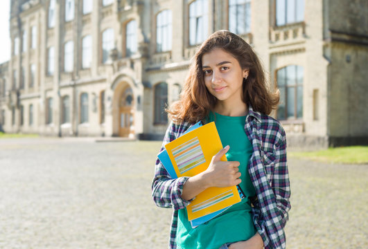 Portrait of an Indian student girl who is smiling holds books near the college. Young brunette woman with textbooks.