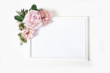 Obraz na płótnie Canvas Wedding, birthday sign board mock-up scene. Blank white wooden frame. Decorative floral corner. Green leaves, pink peony, roses and wax flowers. White table background. Flat lay, top view.