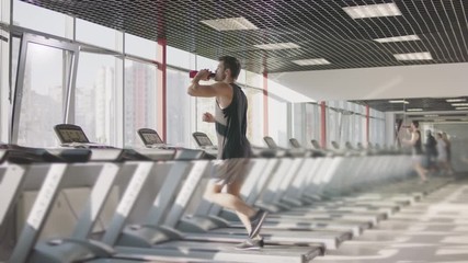 Running man drinking water on treadmill machine in gym club.