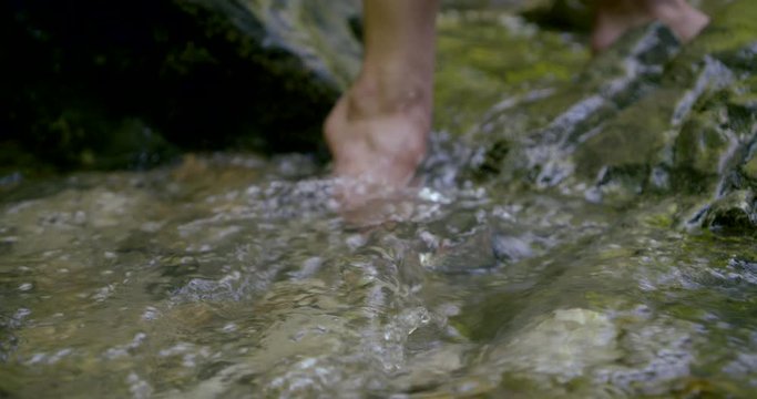 Close-up of female feet that urinate in the stream. Around water stones.