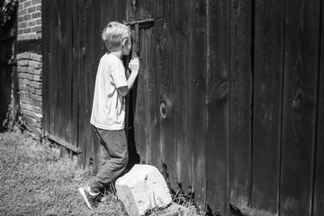 Children's curiosity - boy looking throw the hol in the gate to the shed