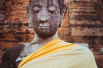 Buddha, a crumbling statue with the peaceful, meditative face and closed eyes, covered with orange...