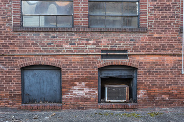 Back of red brick building with covered windows in alley