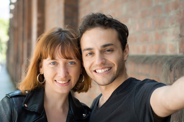 Young couple taking selfie with mobile phone outdoors.