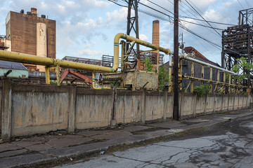 Naklejka premium Large pipes running along a large concrete wall in front of an abandoned factory