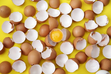 Flat lay Organic broken egg with a yolk in the middle of the egg shell on a yellow background. Background and texture. Protein in food. Easter. The ingredients. Top view.