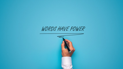 Male hand writing a Words have power sign with black marker on blue background.
