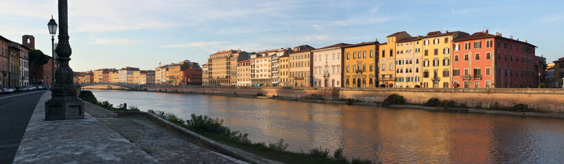 Fototapeta na wymiar Panoramic view of Arno river with palazzo facades in Pisa, Italy, on a sunny evening