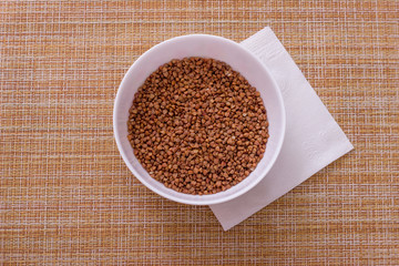 Bowl of raw buckwheat and napkin on granny background, top view