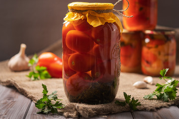 Homemade jars of pickled tomatoes on a rustic wooden background. Pickled and canned product. Next other for cooking. 
