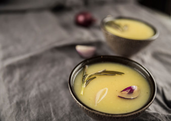 Сream soup with rosemary, potatoes and onions in brown soup plates.