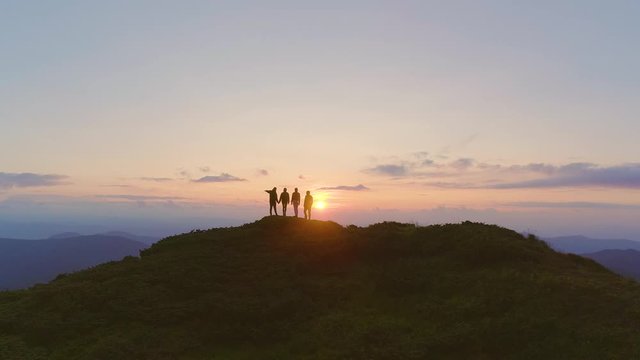 The four friends standing on the mountain against a beautiful sunset