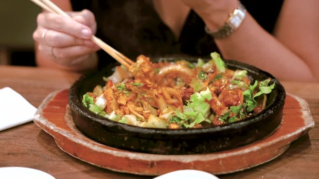 Person eating spicy grilled octopus dish at Korean restaurant