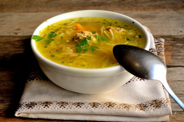 Homemade soup with meatballs and noodles, folk napkin on a wooden table.