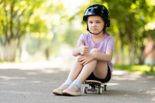 The little one sits on a skateboard, shows a class sign, with a funny expression on her face.