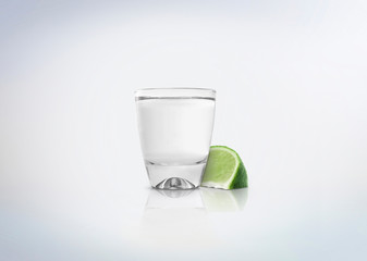 Silver shot of tequila. Alcoholic distilled beverage with slice of lemon / lime on the side. Isolated on white background.