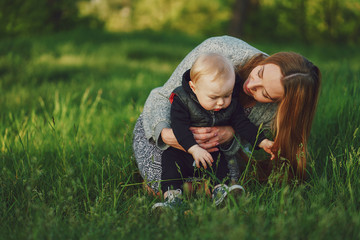 Fototapeta premium beautiful long-haired young mother in the summer sunshine park are sitting and playing with little cute sons