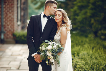 Beautiful bride in a long white dress. Handsome groom in a black suit. Couple in a summer park