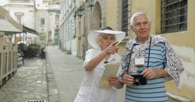 Senior male and female tourists standing with a map in hands looking for route