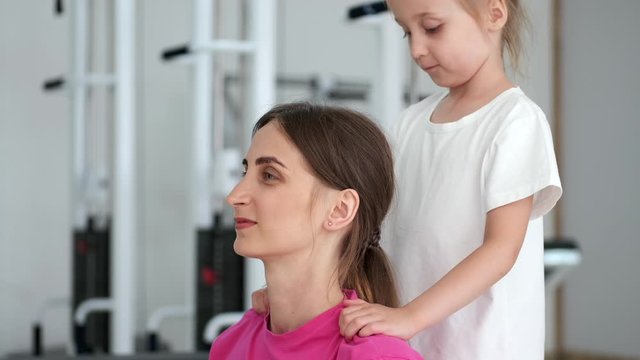 little girl massaging her mom's shoulders at the gym