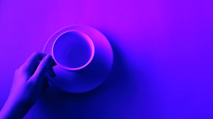 Cup of tea, coffee below neon light. With copy space to insert text. Wide screen view. It represents youth which works and have to be profitable