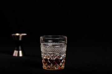 A shot of whiskey in a vintage glass with a measuring jigger behind