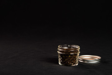 A small jar of black tea isolated on a black background