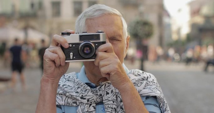 Senior male tourist exploring town and makes a photo with retro photo camera