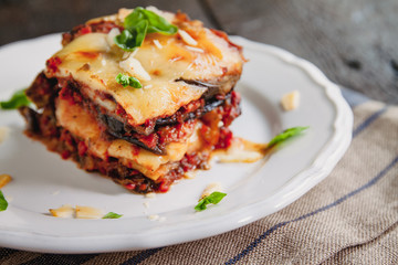 tradicional Parmigiana di melanzane: baked eggplant - italy, sicily cousine.Baked eggplant with cheese, tomatoes and spices on a white plate. A dish of eggplant is on a wooden table - 284609785