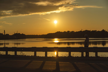 Silhouette of man sitting on a roadside looking out on a a lake with sunset.