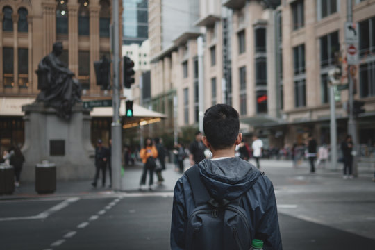 Young Man With Headphones In Waiting To Cross The Road In The City.