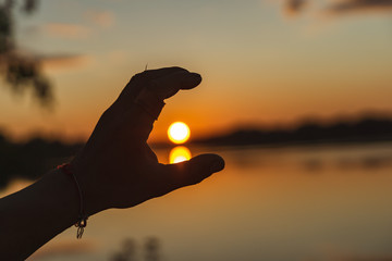 hands holding the sun at dawn. hand framing view distant over sunset