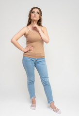Photo full-length portrait of a pretty brunette woman girl with long beautiful curly hair on a white background in a t-shirt and blue jeans. Talking while standing in front of the camera.