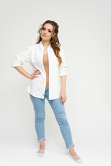 Photo full-length portrait of a pretty brunette woman girl with long beautiful curly hair on a white background in a white shirt and blue jeans. Talking while standing in front of the camera.