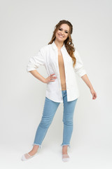 Photo full-length portrait of a pretty brunette woman girl with long beautiful curly hair on a white background in a white shirt and blue jeans. Talking while standing in front of the camera.