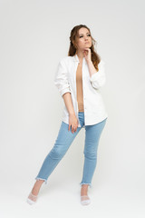 Photo full-length portrait of a pretty brunette woman girl with long beautiful curly hair on a white background in a white shirt and blue jeans. Talking while standing in front of the camera.