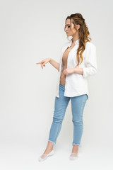 Photo full-length portrait of a pretty brunette woman girl with long beautiful curly hair on a white background in a white shirt and blue jeans. Talking while standing in front of the camera.