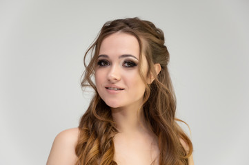 Naklejka premium Close-up photo portrait of a pretty brunette woman girl with long beautiful curly hair on a white background. Standing in front of the camera