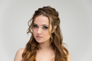 Fototapeta premium Close-up photo portrait of a pretty brunette woman girl with long beautiful curly hair on a white background. Standing in front of the camera