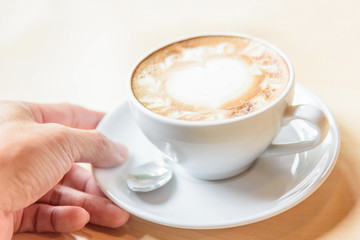 take the Hot coffee in hand / hot cappuccino with nice pattern in hand and wood background