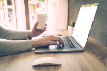 Woman holding coffee and using laptop on wooden table in office