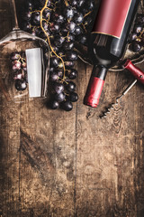 Red wine bottle and glass with grapes on rustic wooden background. Top view. Border. Copy space....