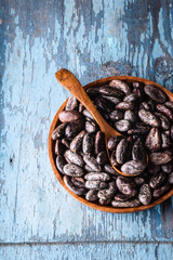 Organic raw dry cocoa beans in wooden bowl on blue old rustic background