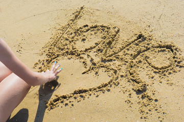 Girl at the beach drawing hearts on a sand