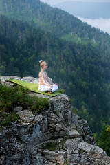 Naklejka na ściany i meble Young woman practicing yoga outdoors harmony with nature. Girl meditating sitting in lotus pose on stone